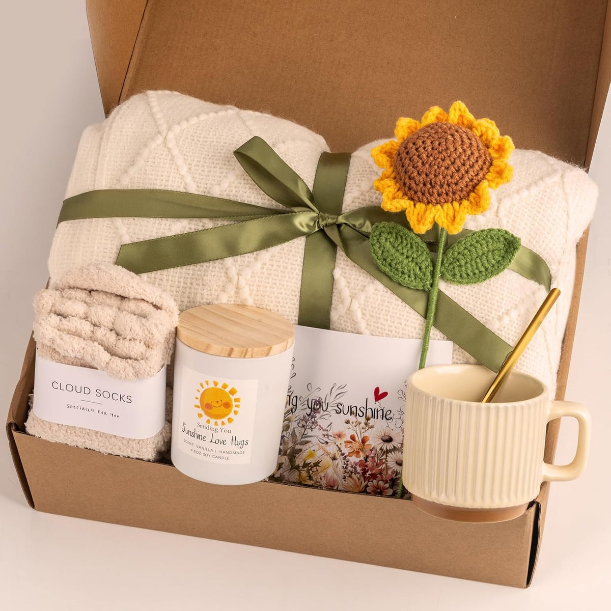 8 included items: knitted tassel blanket, fuzzy socks, ceramic mug, hand-woven sunflower, metal spoon, soy wax candle, gift card, and gift box